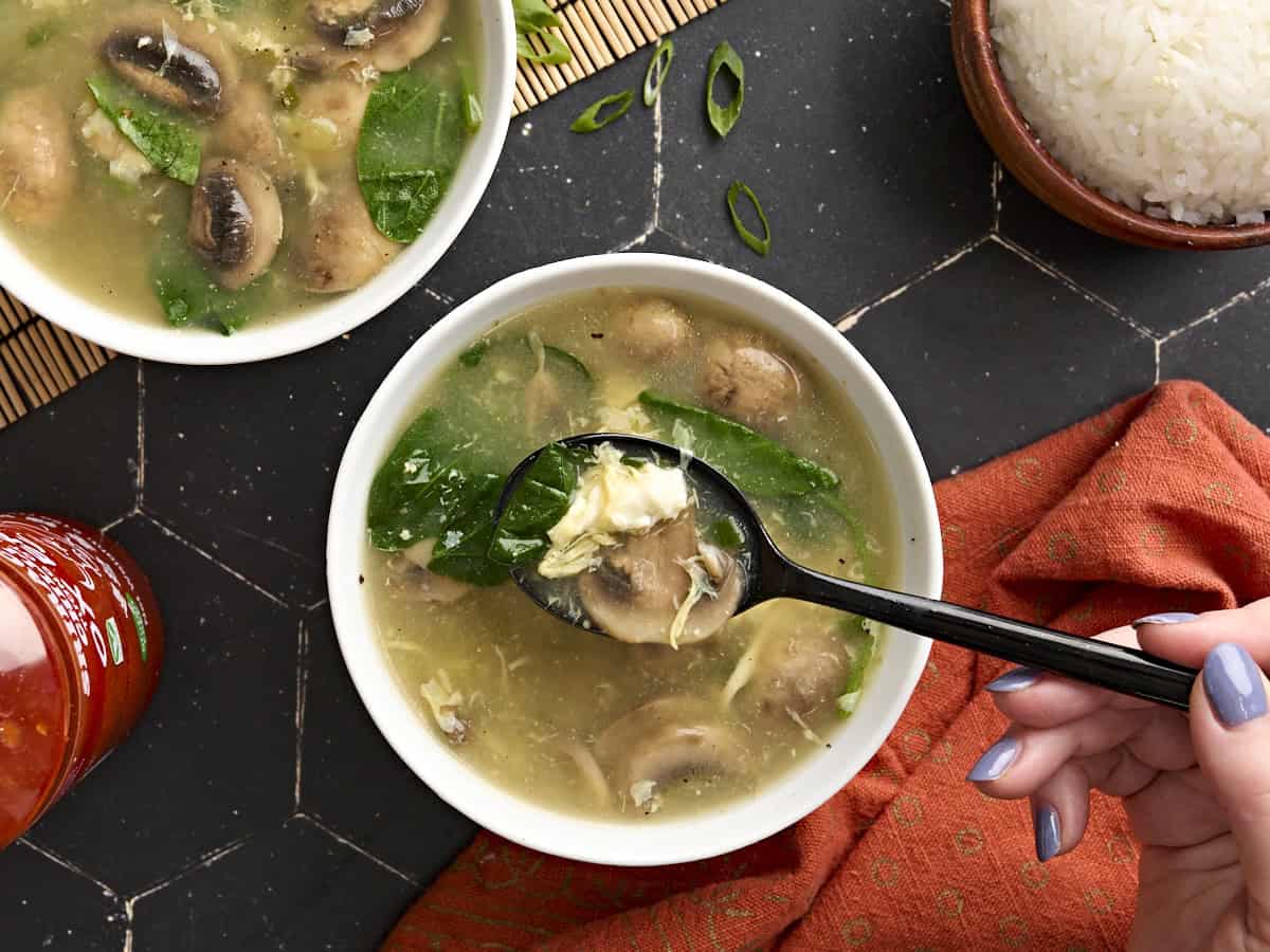 Overhead view of a bowl of egg drop soup with some on a black spoon.