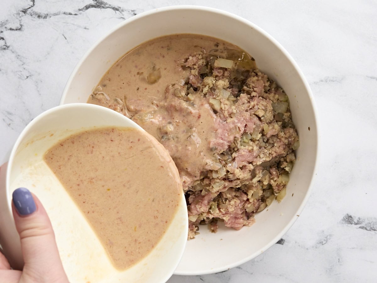 The wet egg and milk mix being poured into a bowl of ground turkey, veggies, and breadcrumbs.