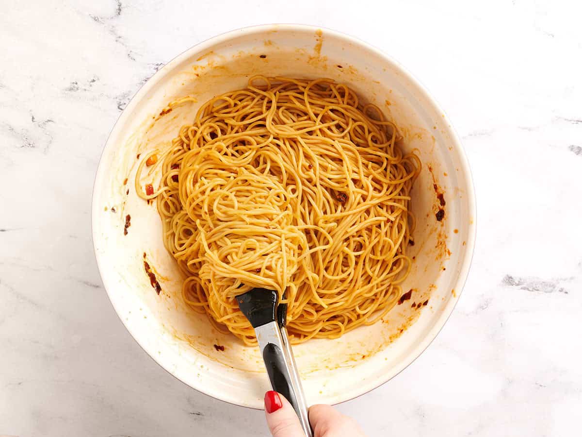 Dan dan noodles being tossed in sauce in a bowl.