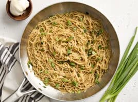 Overhead view of garlic noodles in a skillet, topped with sliced green onions.