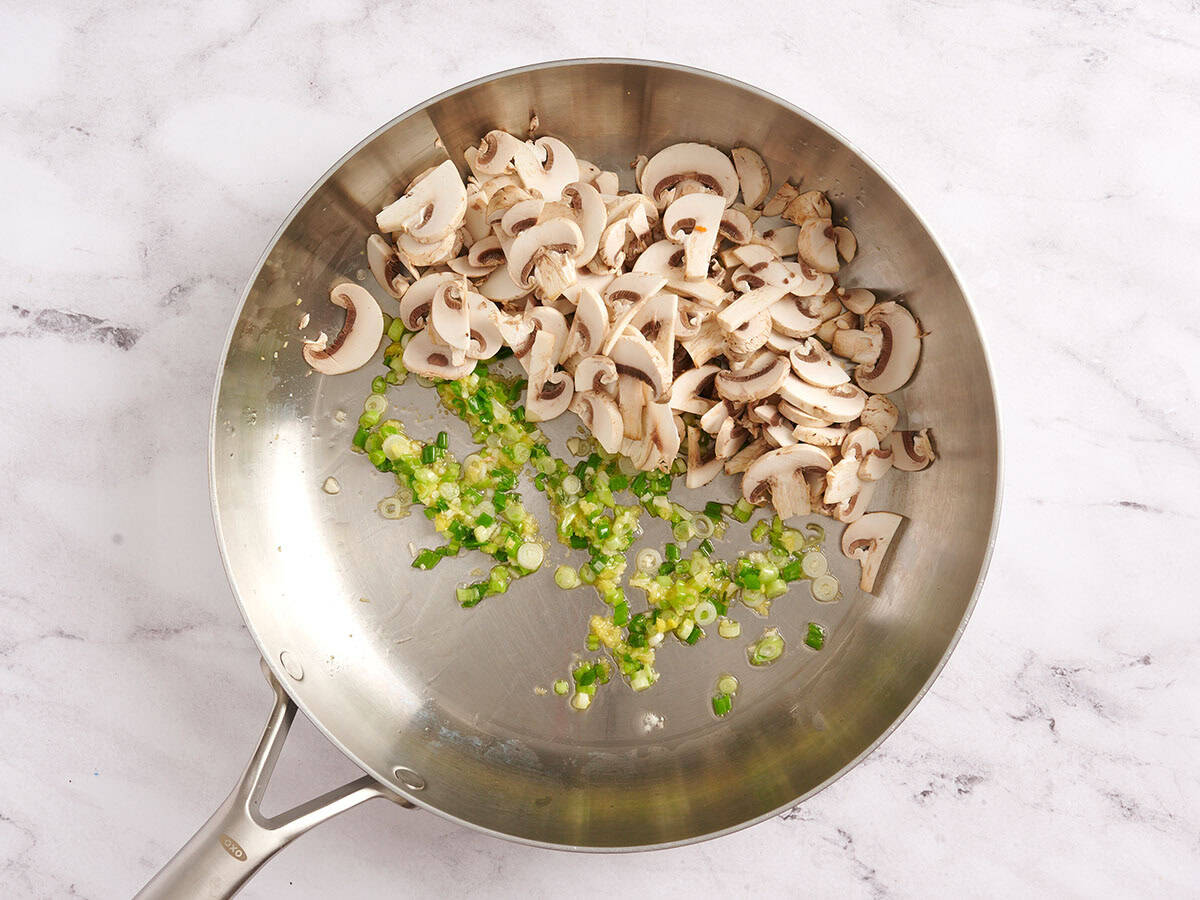Mushrooms in a skillet with sauteed green onions.