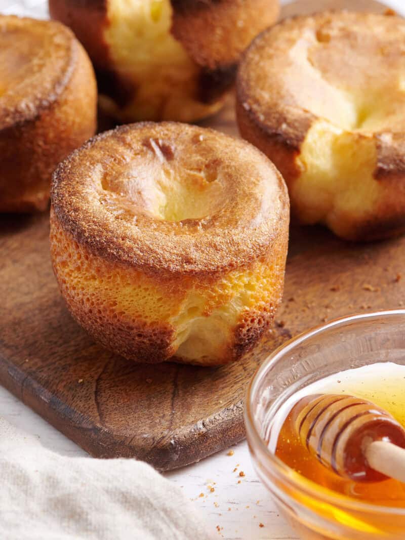 Popover on a wooden cutting board with a bowl of honey.
