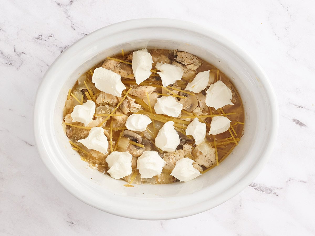 Noodles and cream cheese added to a slow cooker of chicken tetrazzini.