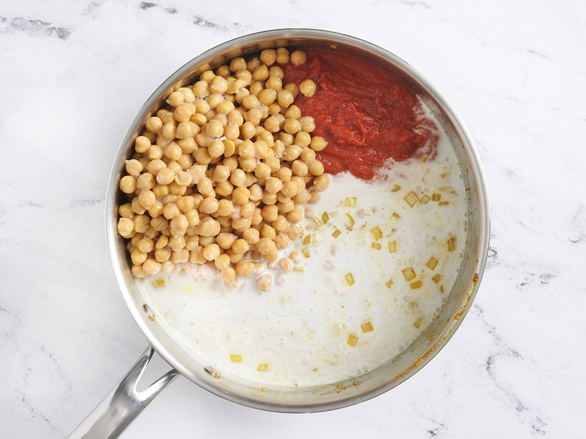 Coconut milk, chickpeas, and tomato in a skillet.