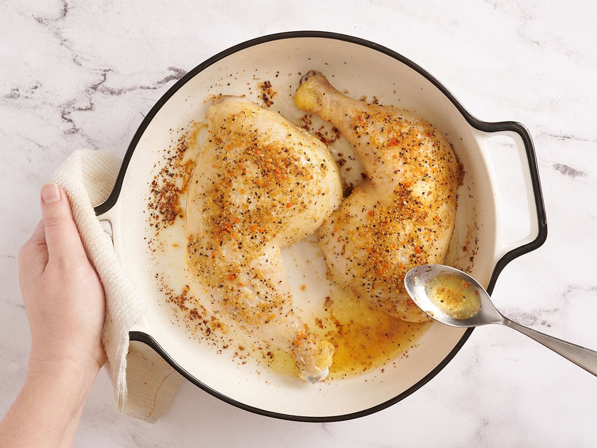A spoon basting chicken legs after one hour of baking.