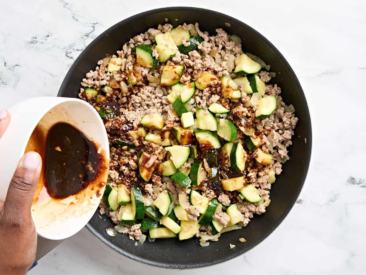 A bowl pouring a homemade soy sauce and brown sugar sauce over a zucchini ground turkey skillet dinner.