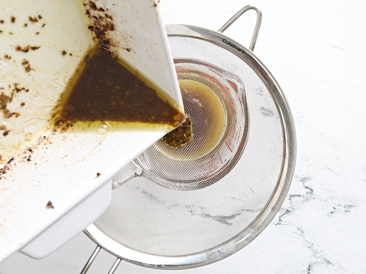 Pouring turkey pan drippings through a fine mesh strainer into a measuring cup.