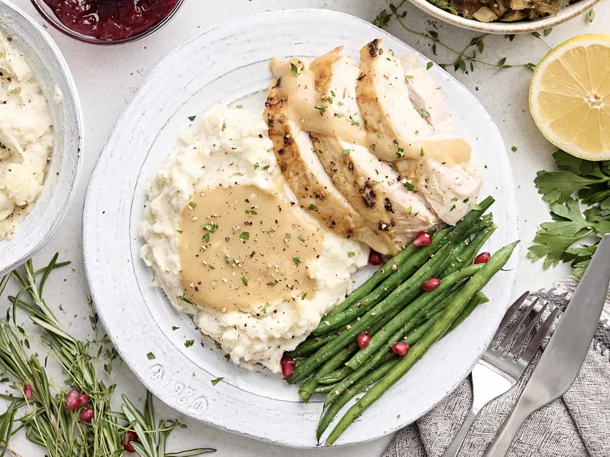 Overhead view of turkey breast, green beans and mashed potatoes topped with turkey gravy.