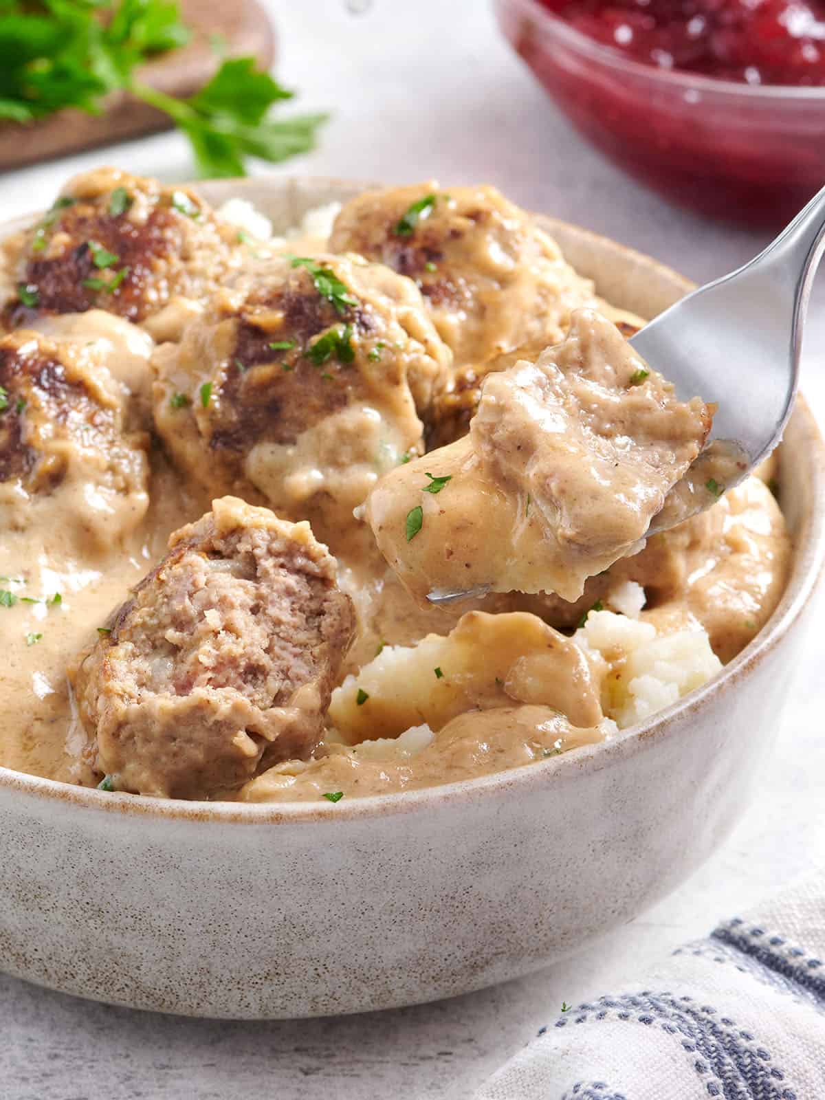 Side view of a bowl of Swedish meatballs with mashed potatoes and a fork taking some.