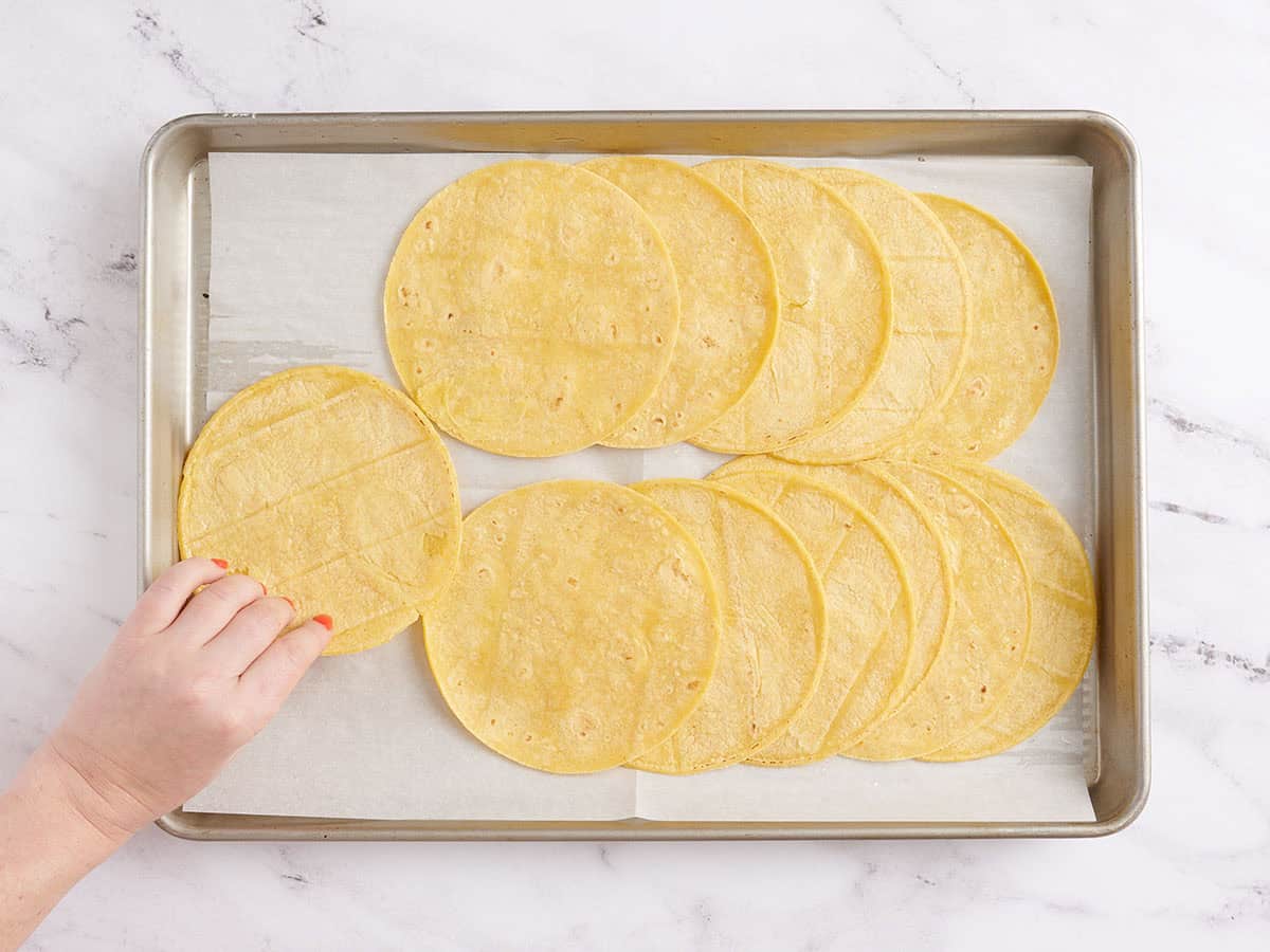 A hand arranging tortillas on a sheet pan.