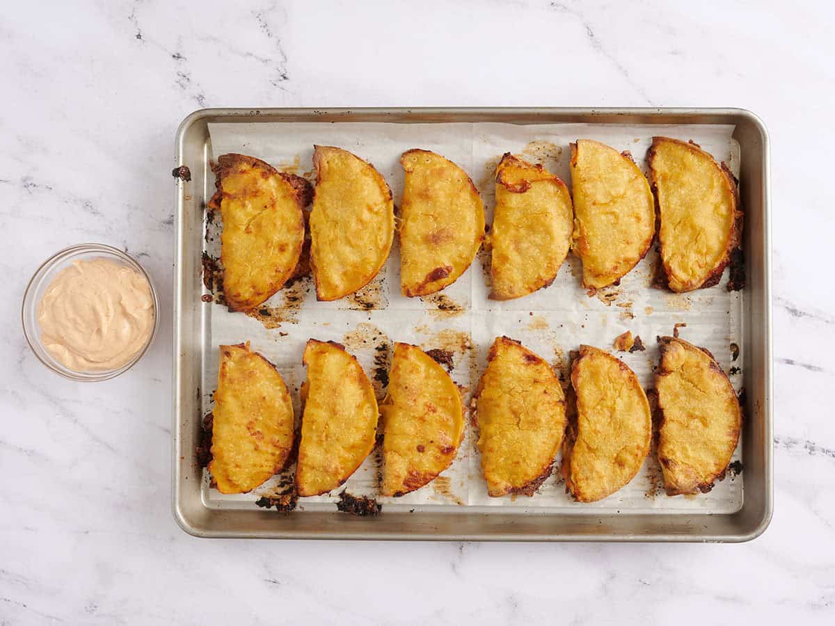 Sheet pan tacos on a baking tray with a bowl of spiced sour cream dipping sauce to the side.