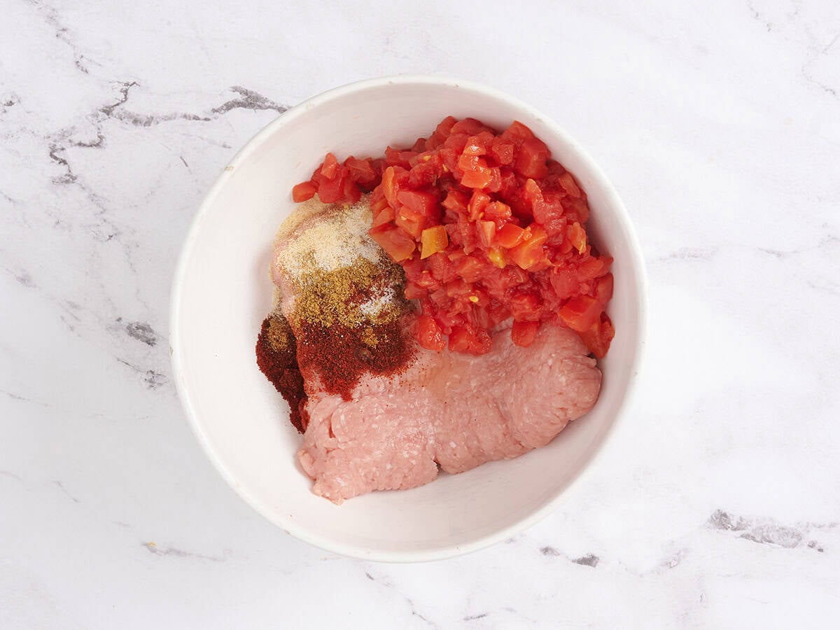 Spices, diced tomatoes, and ground turkey in a mixing bowl.
