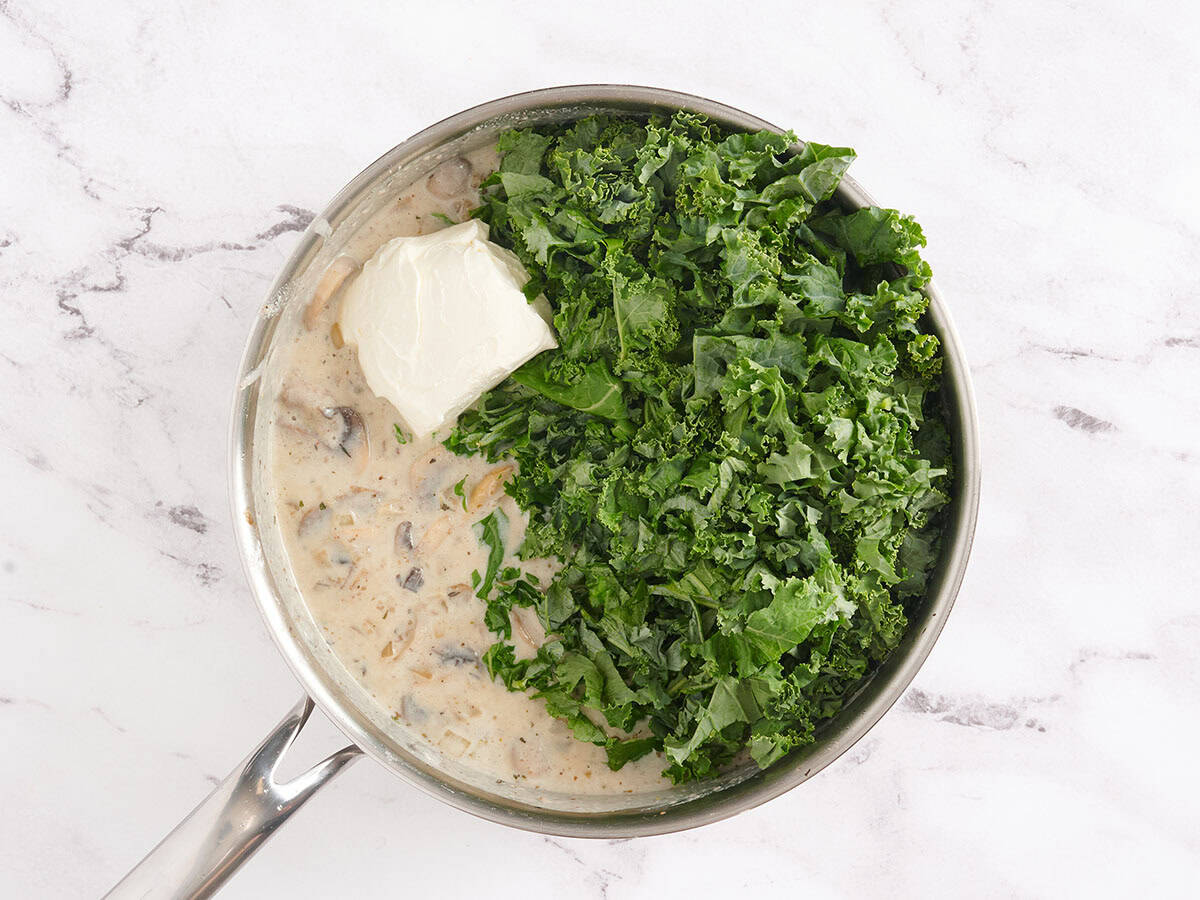 Fresh kale and cream cheese added to a skillet to make the filling for turkey sausage and kale casserole.