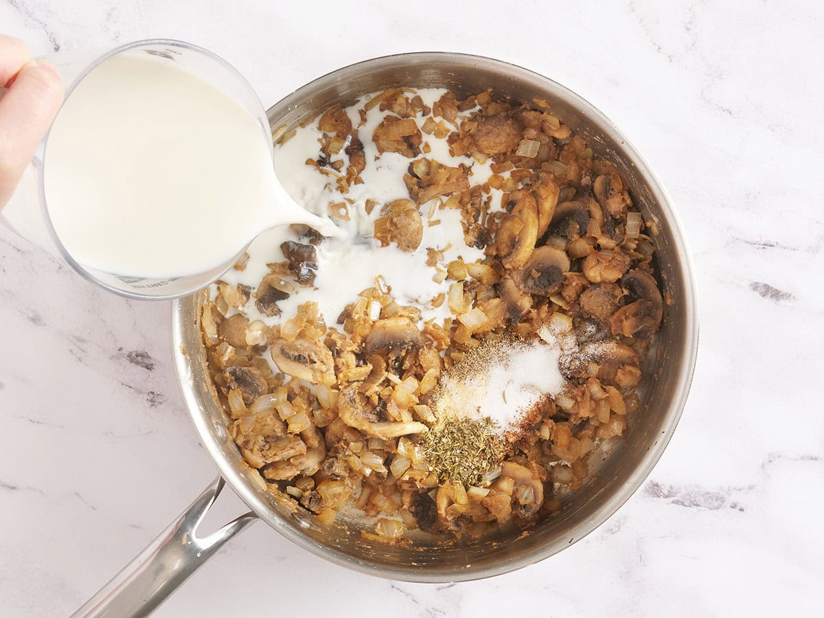 Milk being poured into a skillet to make a creamy mushroom onion sauce.