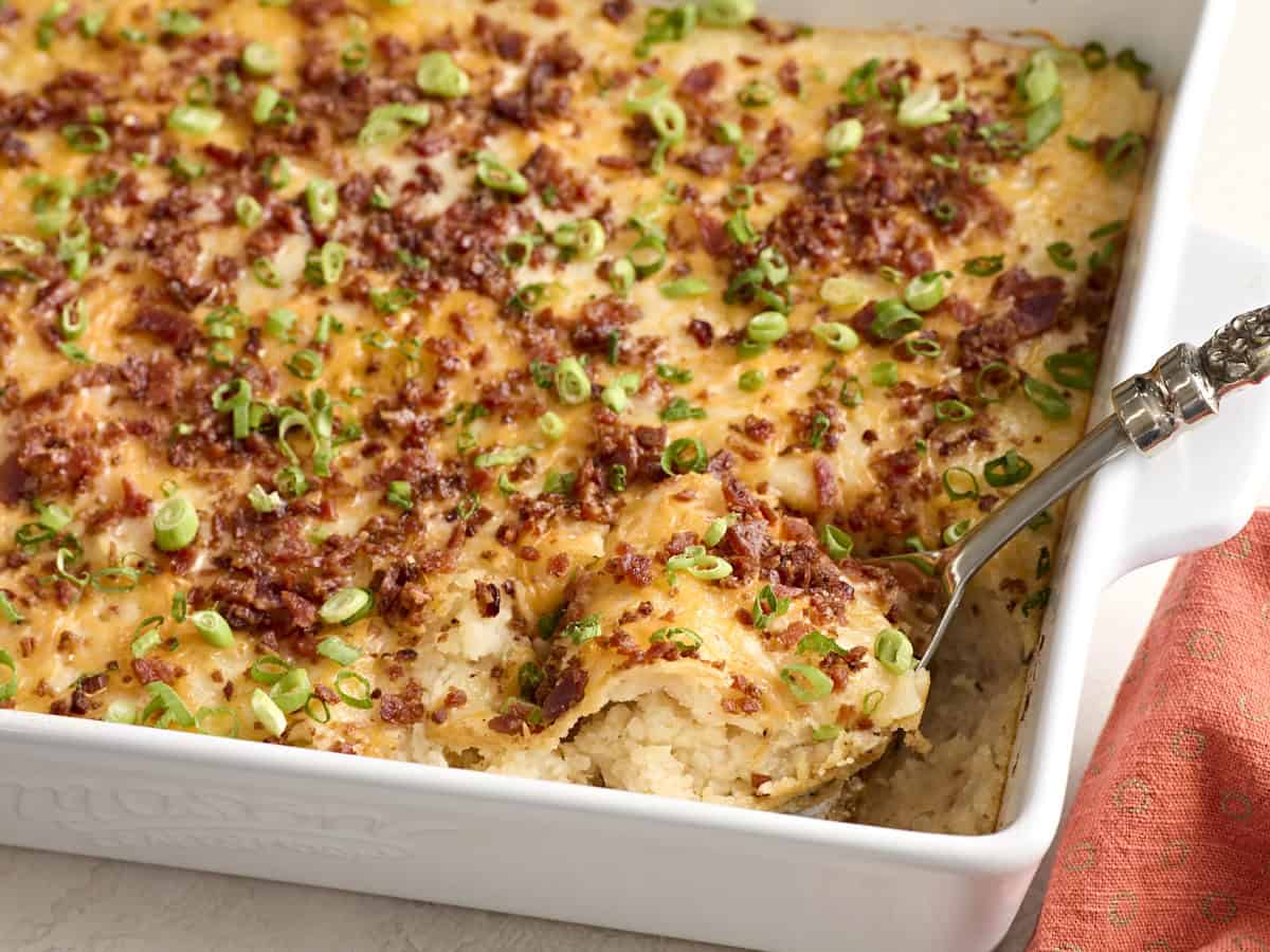 Side view of a spoon taking mashed potato casserole from a baking dish.