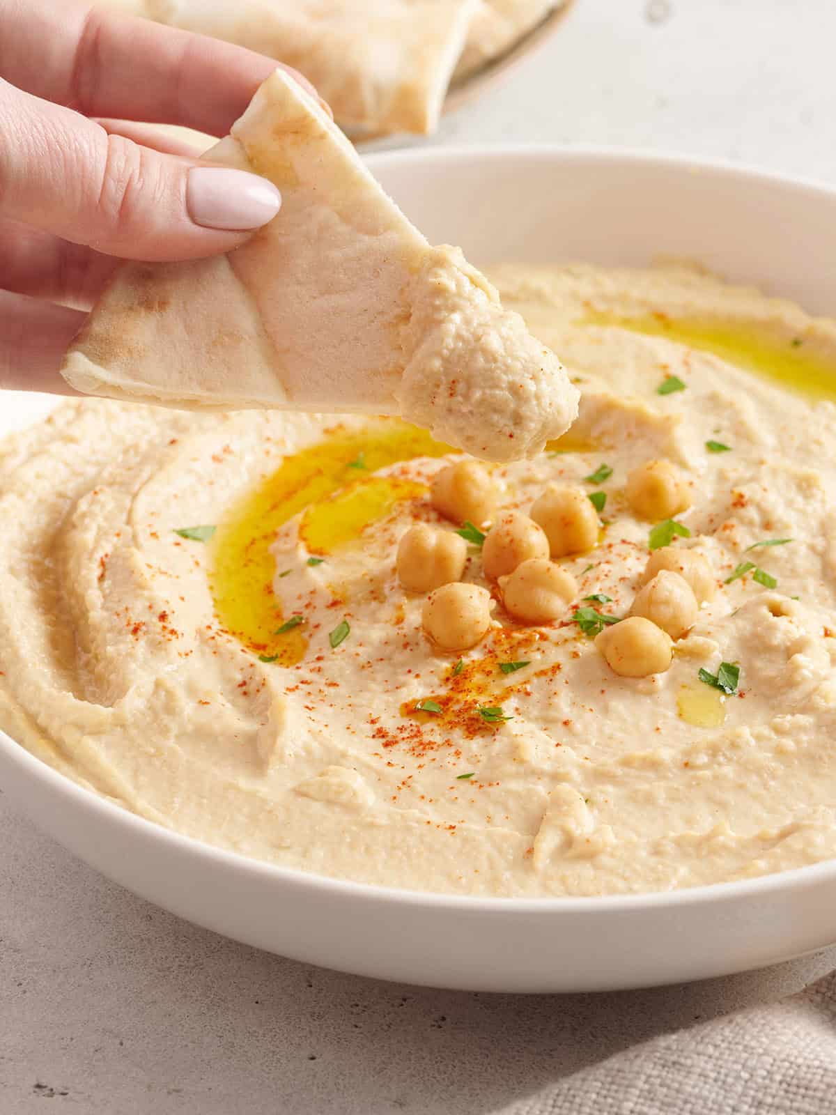 Homemade hummus is quick, easy, and inexpensive, and can be made with several different flavor add-ins. Here are four delicious flavors to try. Budgetbytes.com Side view of a hand holding a chip after being dipped in hummus.