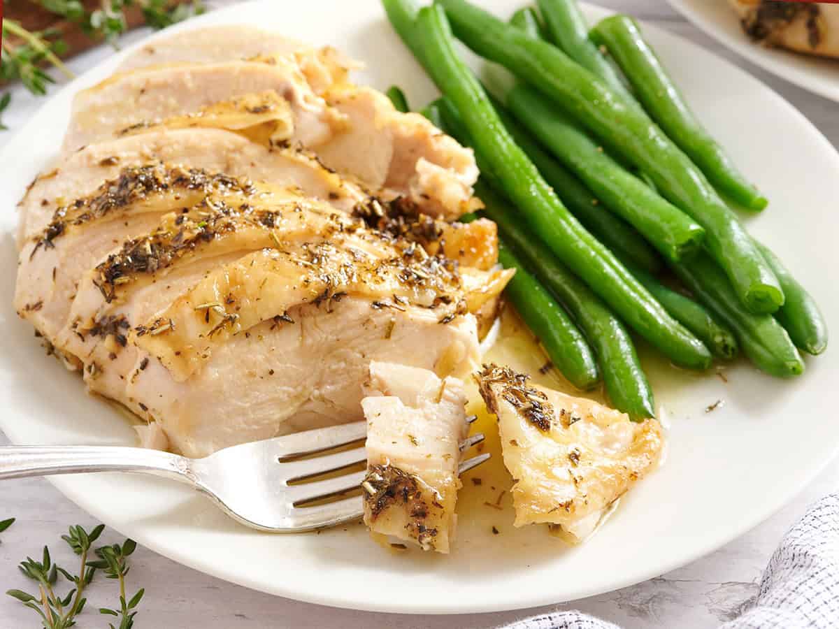 A herb roasted chicken breast with green beans on a plate with a fork.