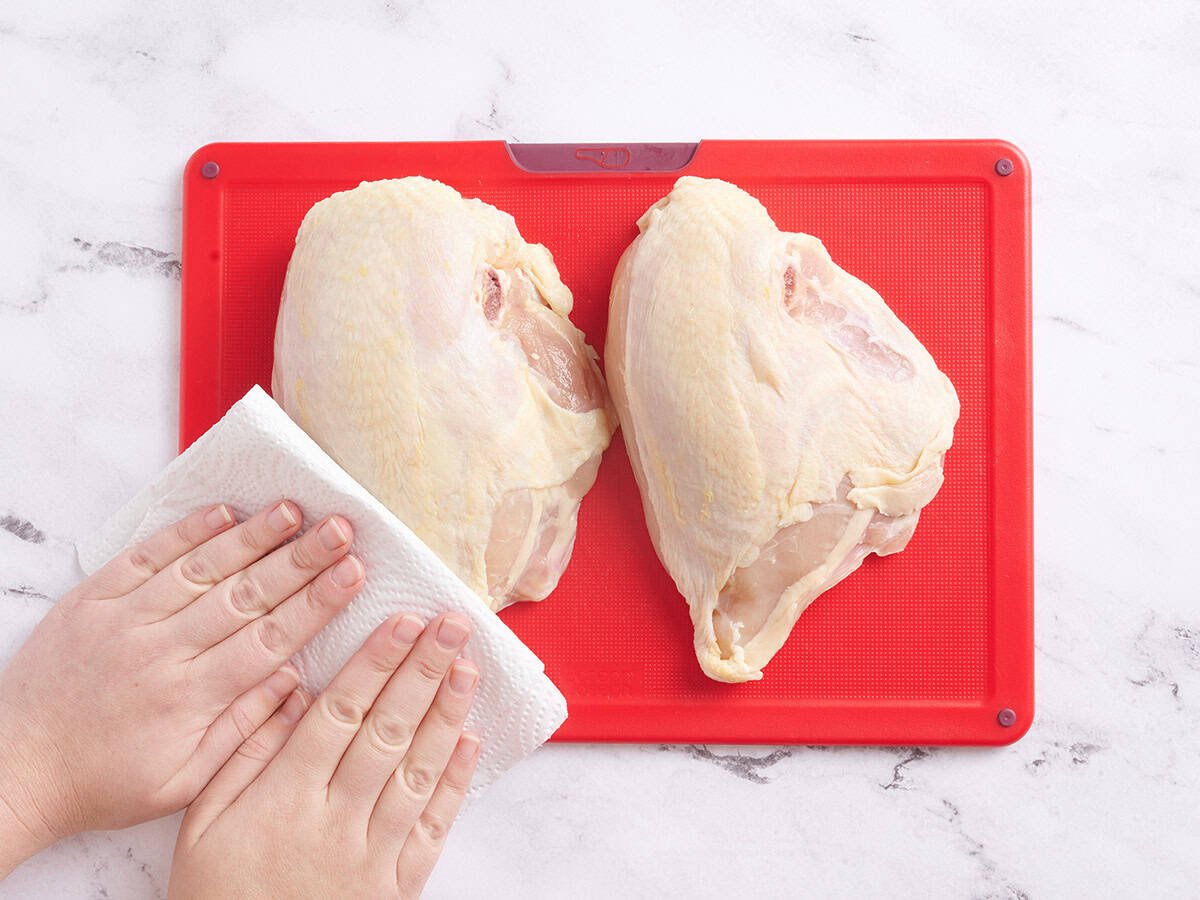 Hands patting chicken breasts with a paper towel.