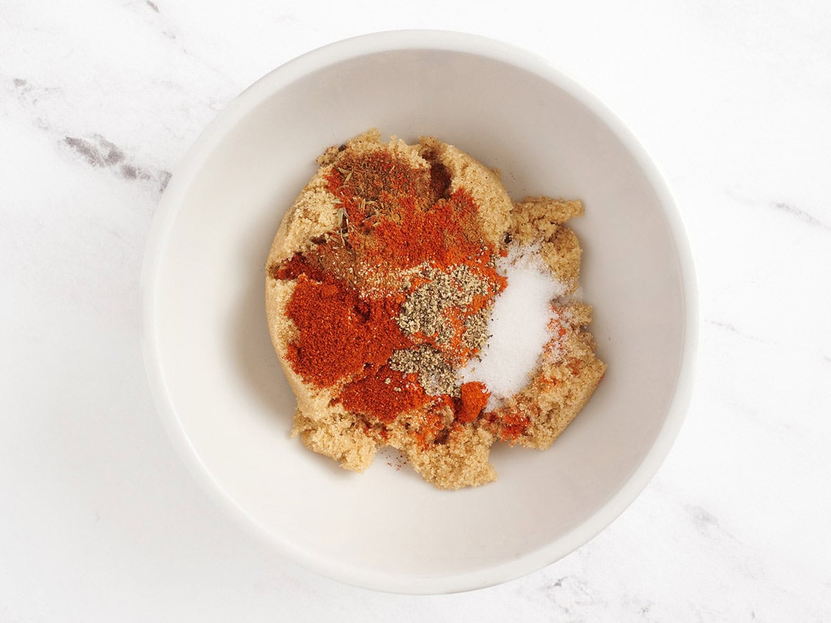 Brown sugar, cayenne, garlic powder, paprika, salt, black pepper, cloves, cinnamon and thyme in a mixing bowl.