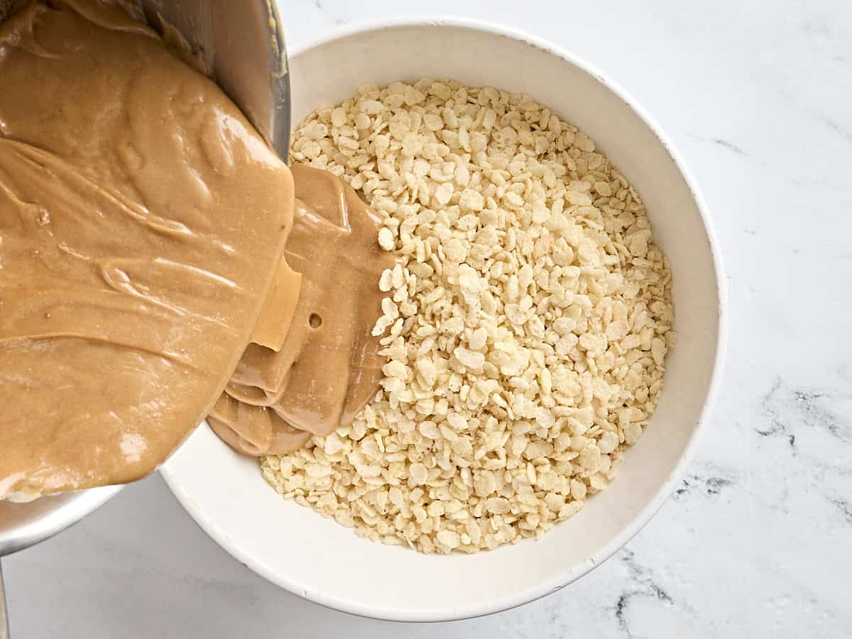 Peanut butter mixture being poured into a bowl of rice krispies to make Scotcharoos.