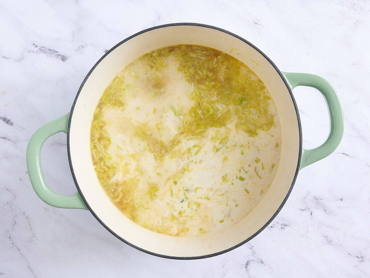 Tempered cream added to potato leek soup in a pot.