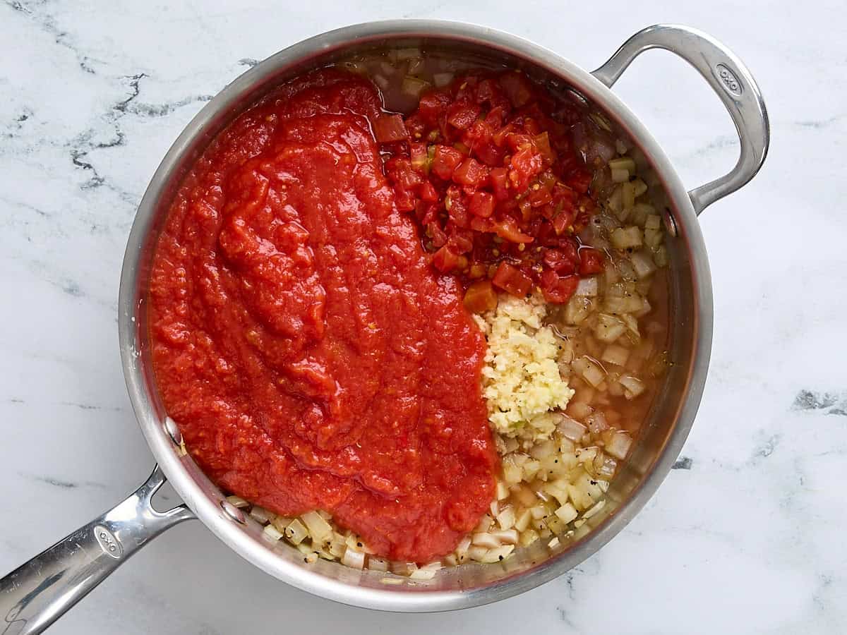 Crushed tomatoes, diced tomatoes with chiles, and garlic added to a skillet of sauteed onions.
