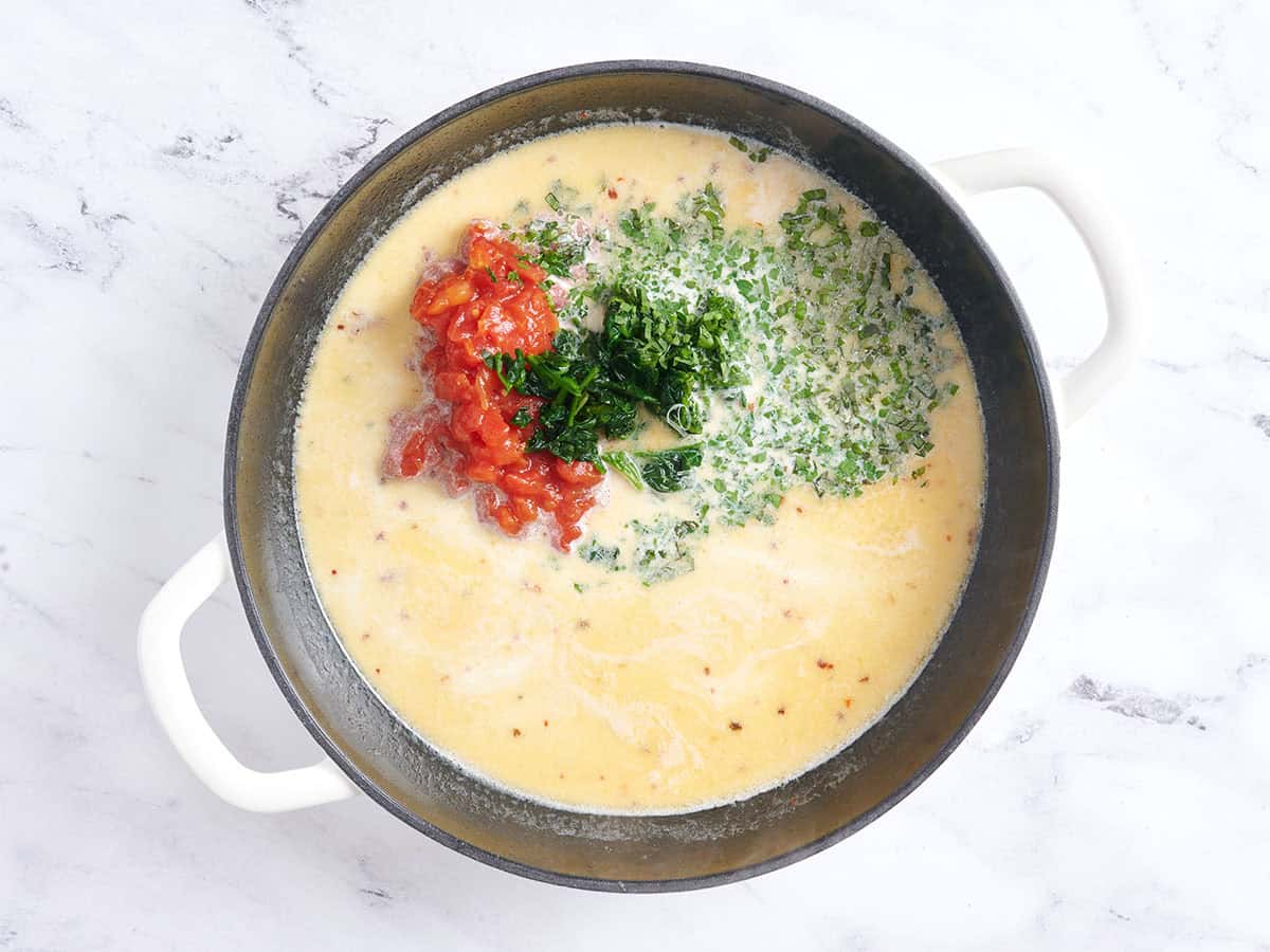 Tomatoes, spinach, herbs and parm added to the sauce for marry me meatballs in a pan.