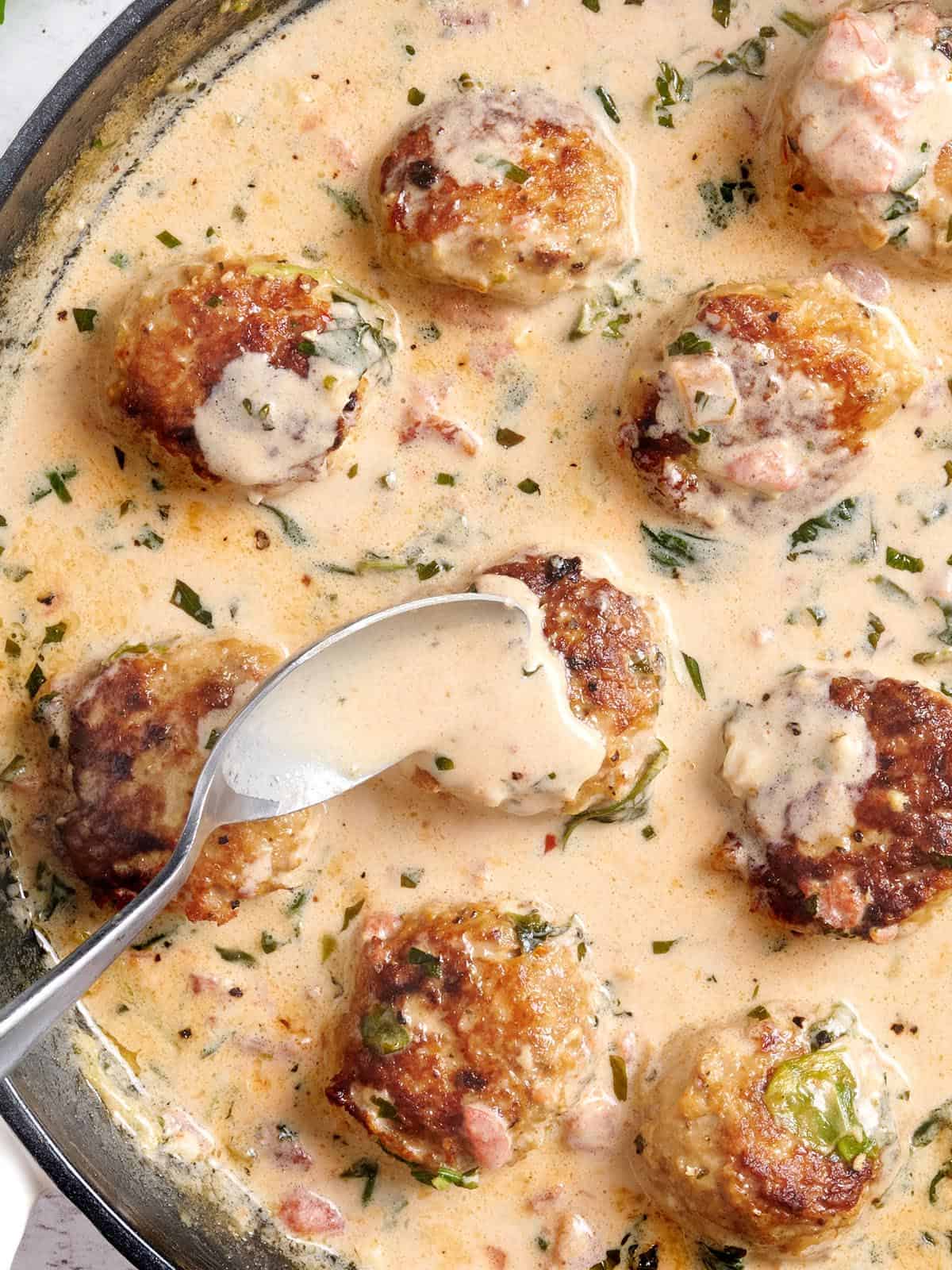 Overhead view of marry meatballs with a spoon pouring sauce over a meatball.