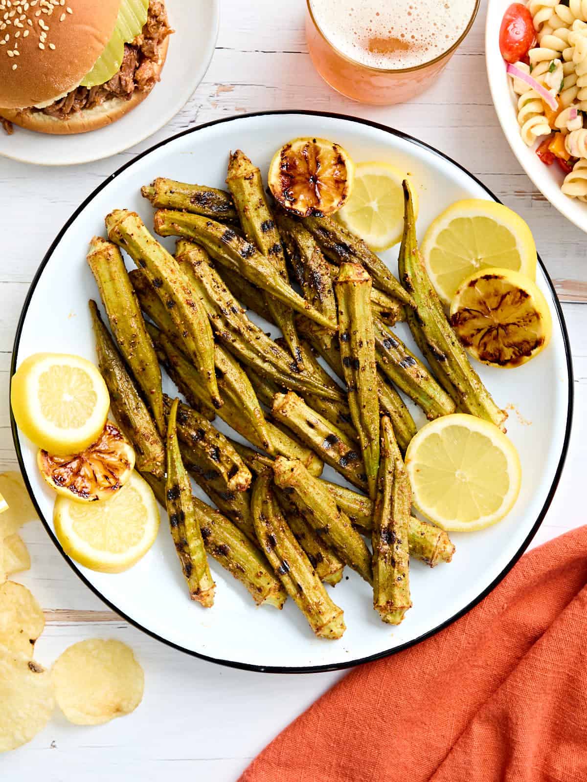Overhead view of grilled okra on a plate with lemon slices.