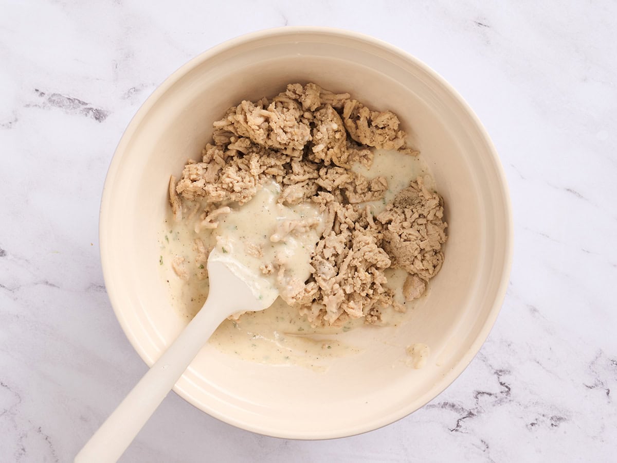 Bechamel sauce added to ground chicken in a bowl.