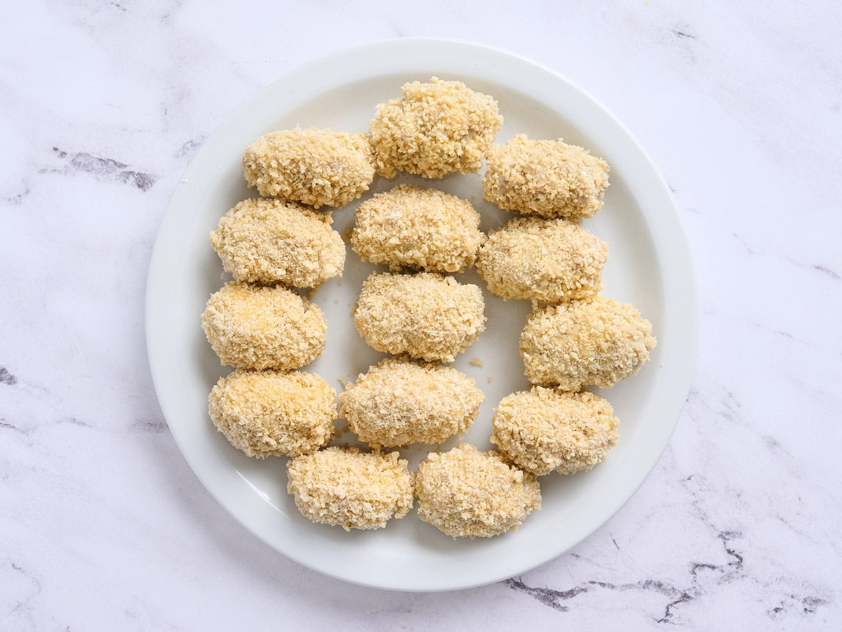 A plate of fully breaded chicken croquettes before frying.