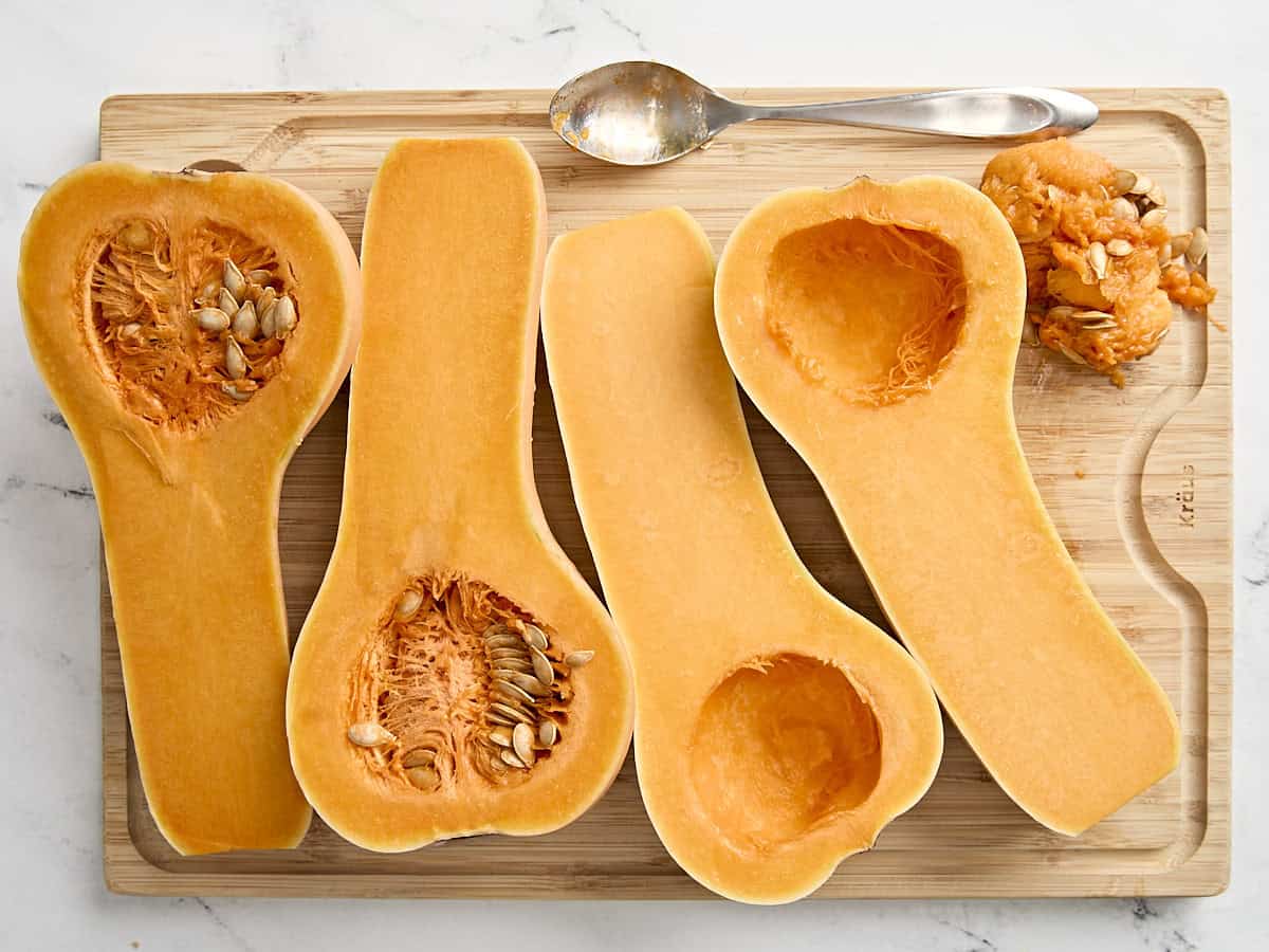 2 butternut squash sliced in half on a wooden chopping board, one with seeds removed.