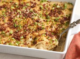 Side view of a spoon taking mashed potato casserole from a baking dish.