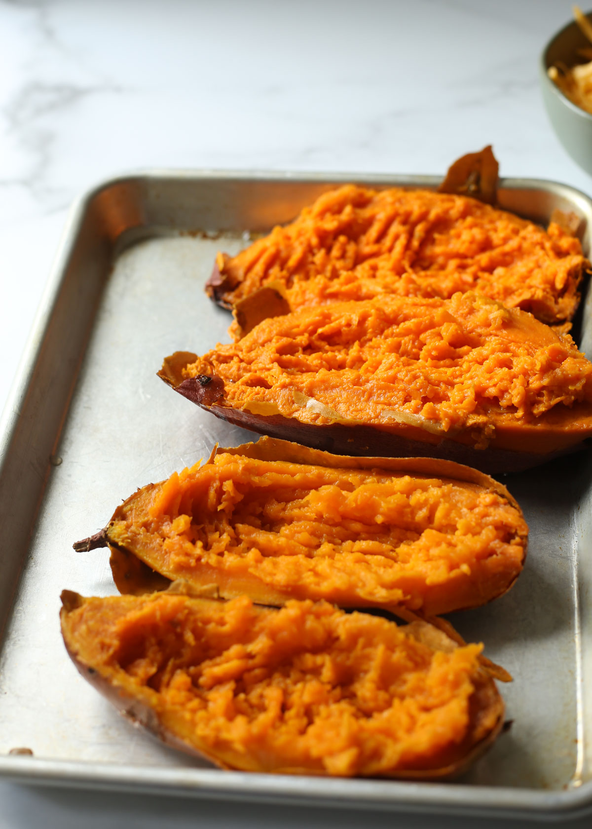 A metal rimmed baking pan with halved baked sweet potatoes