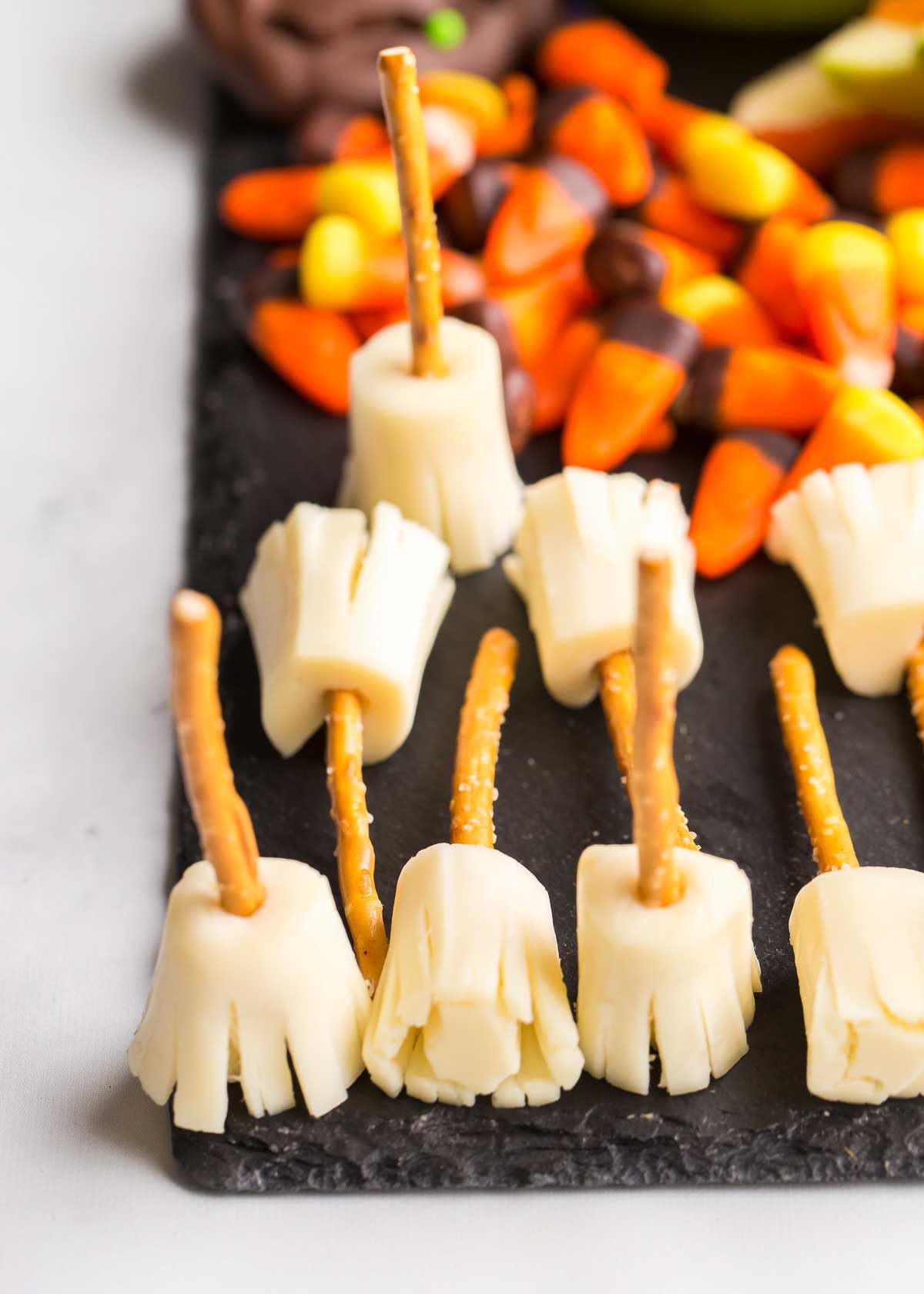 String cheese pretzel broomsticks and candy corns on a slate board.