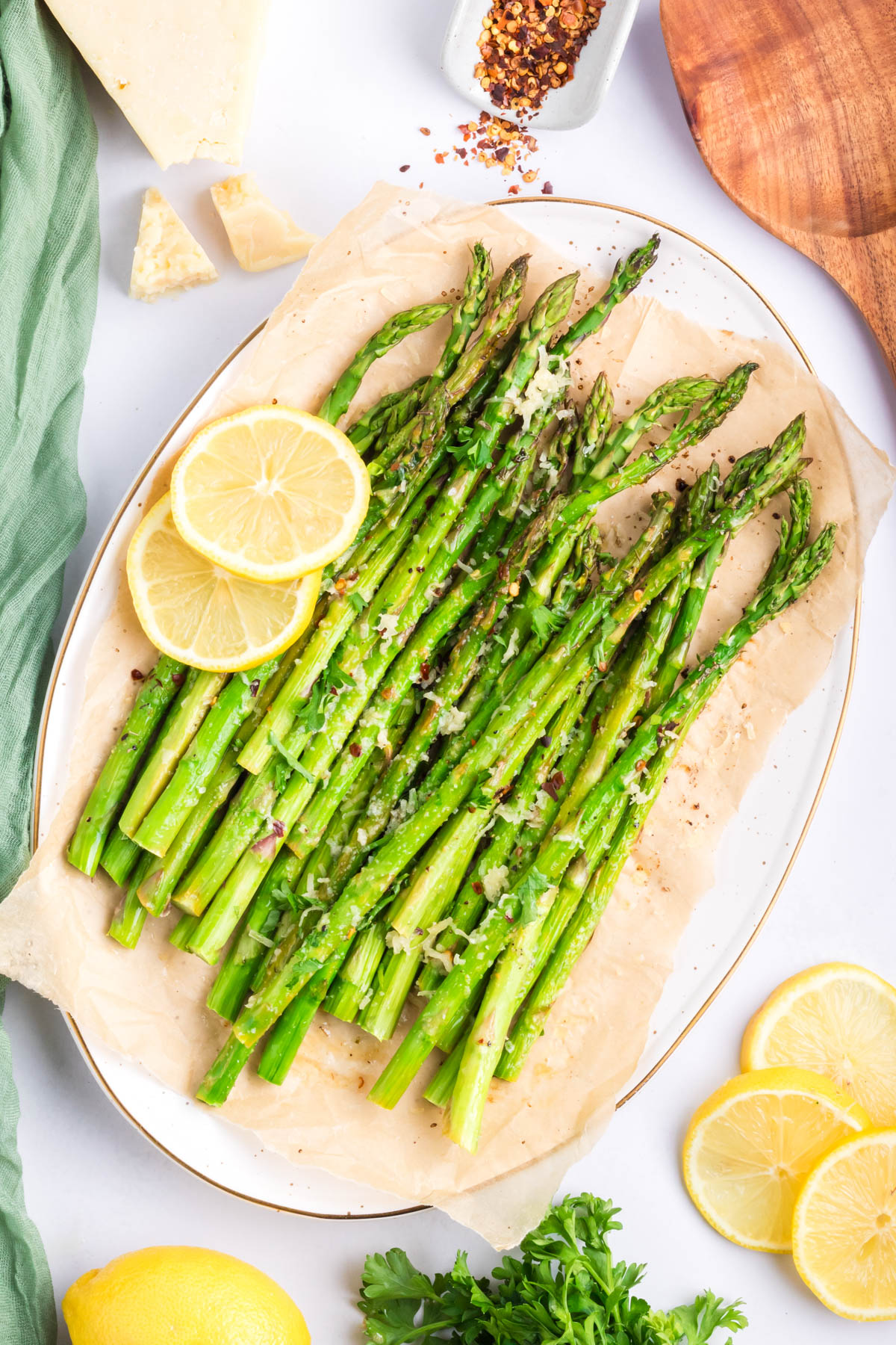 A top view of a white plate of parmesan roasted asparagus. Two slices of lemon are used as a garnish. 
