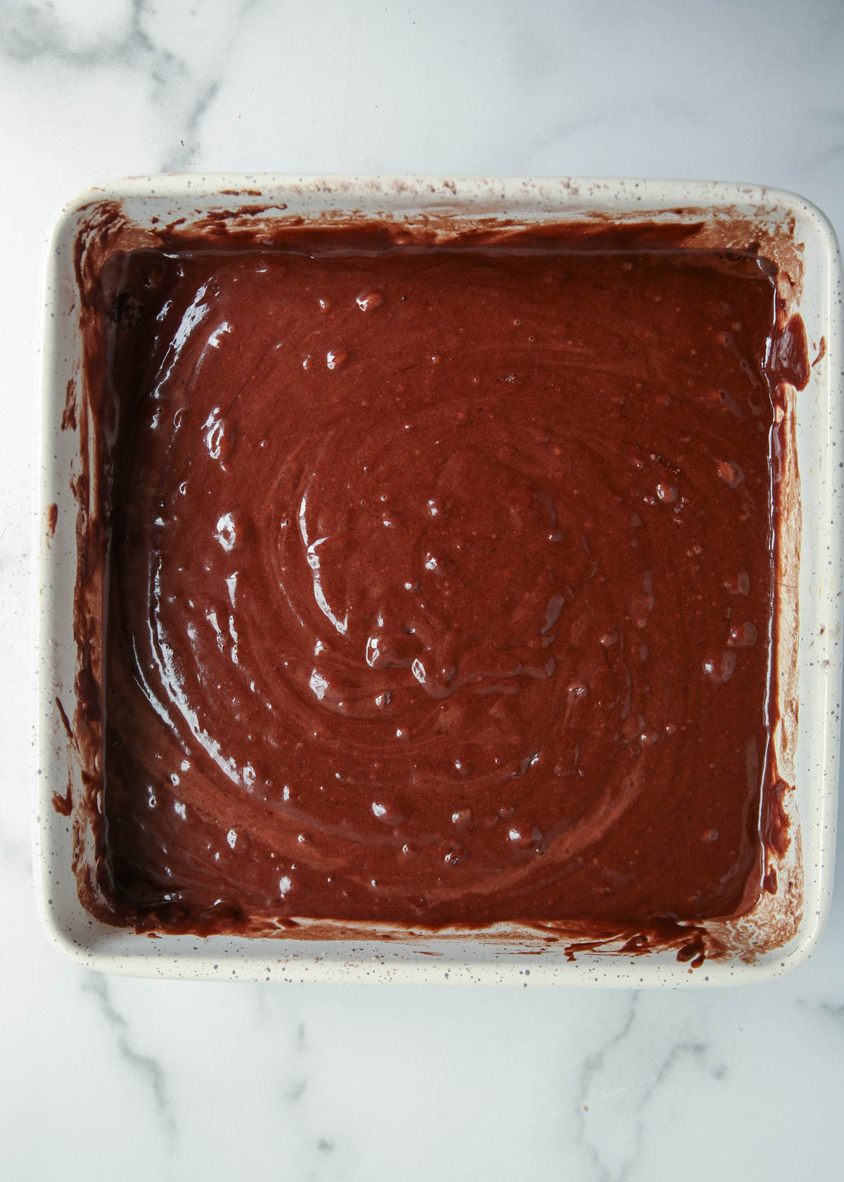 Batter for chocolate wacky cake in a white metal square pan.
