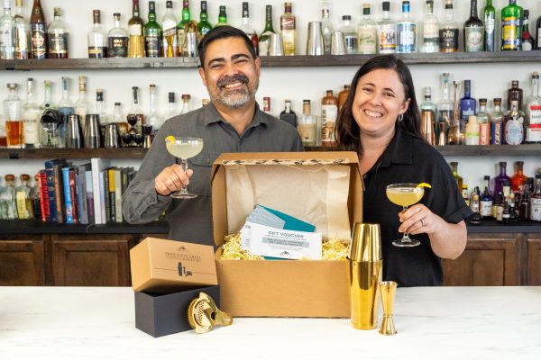 a male female married couple holding cocktails with an open box of barware and gift certificates