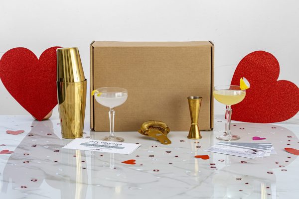 indoor date idea: craft cocktail kit for making two cocktails (box shown with shaker, jigger, strainer, and 2 cocktails), which you can pair with watching your favorite movies under a cozy blanket or with playing your favorite board games